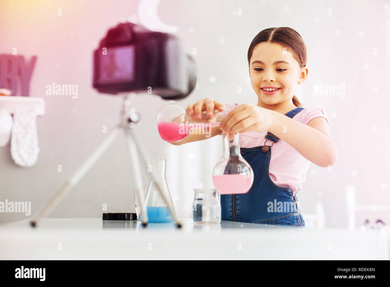Lustig und intelligentes Mädchen tragen Jumpsuit gießen rosa Stoffe in das Reagenzglas Stockfoto