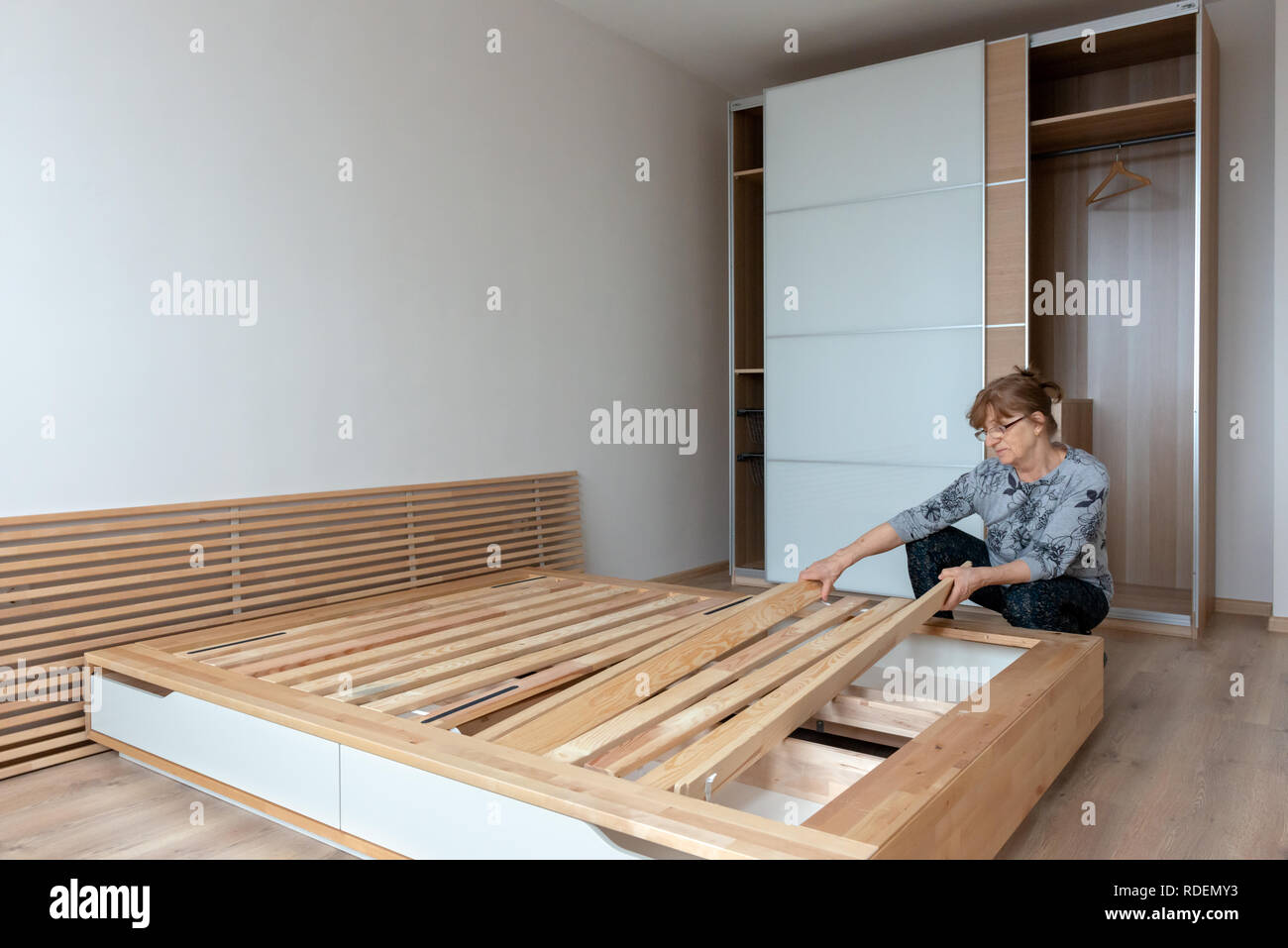 Frau, die IKEA Bio-Holzbett in neu möbliertem Duplex-Schlafzimmer als neues Hauskonzept zusammenstellt Stockfoto
