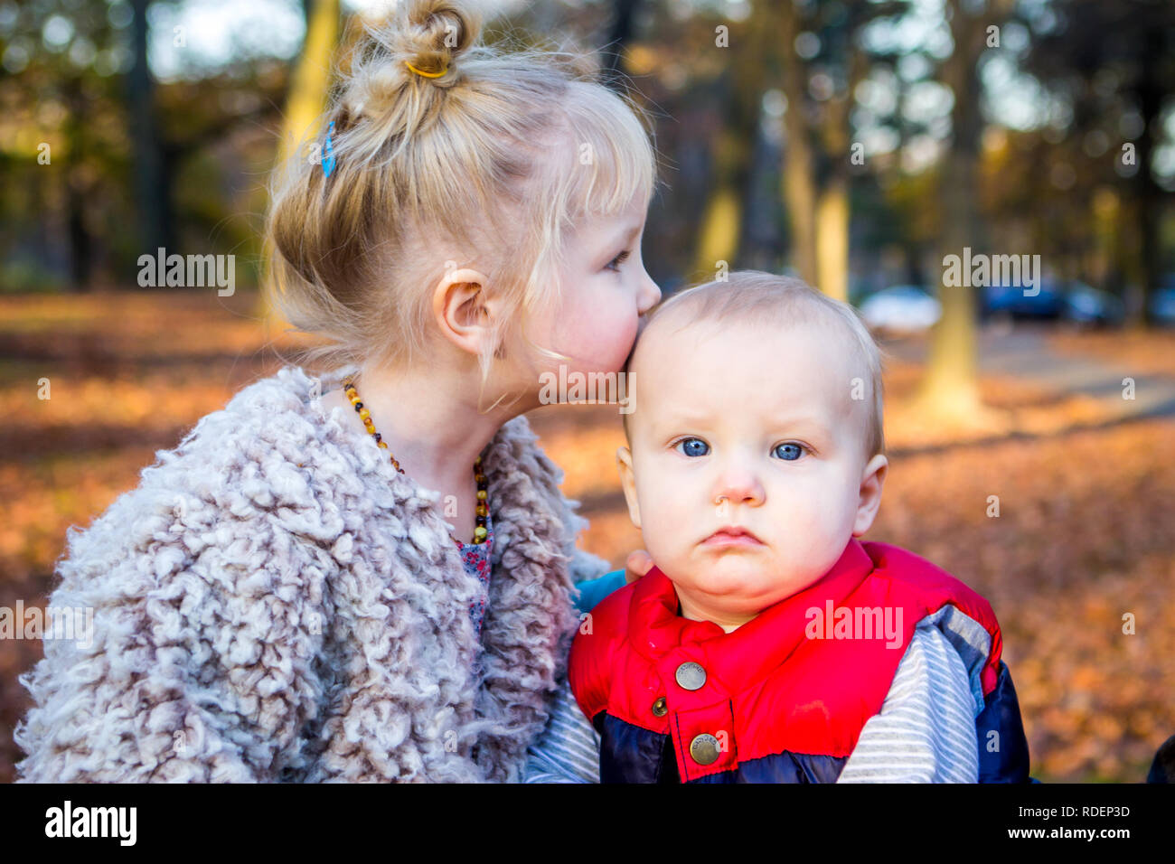 Kaukasischen jungen Geschwister kiss außerhalb im Herbst und im Herbst mit Blättern Stockfoto