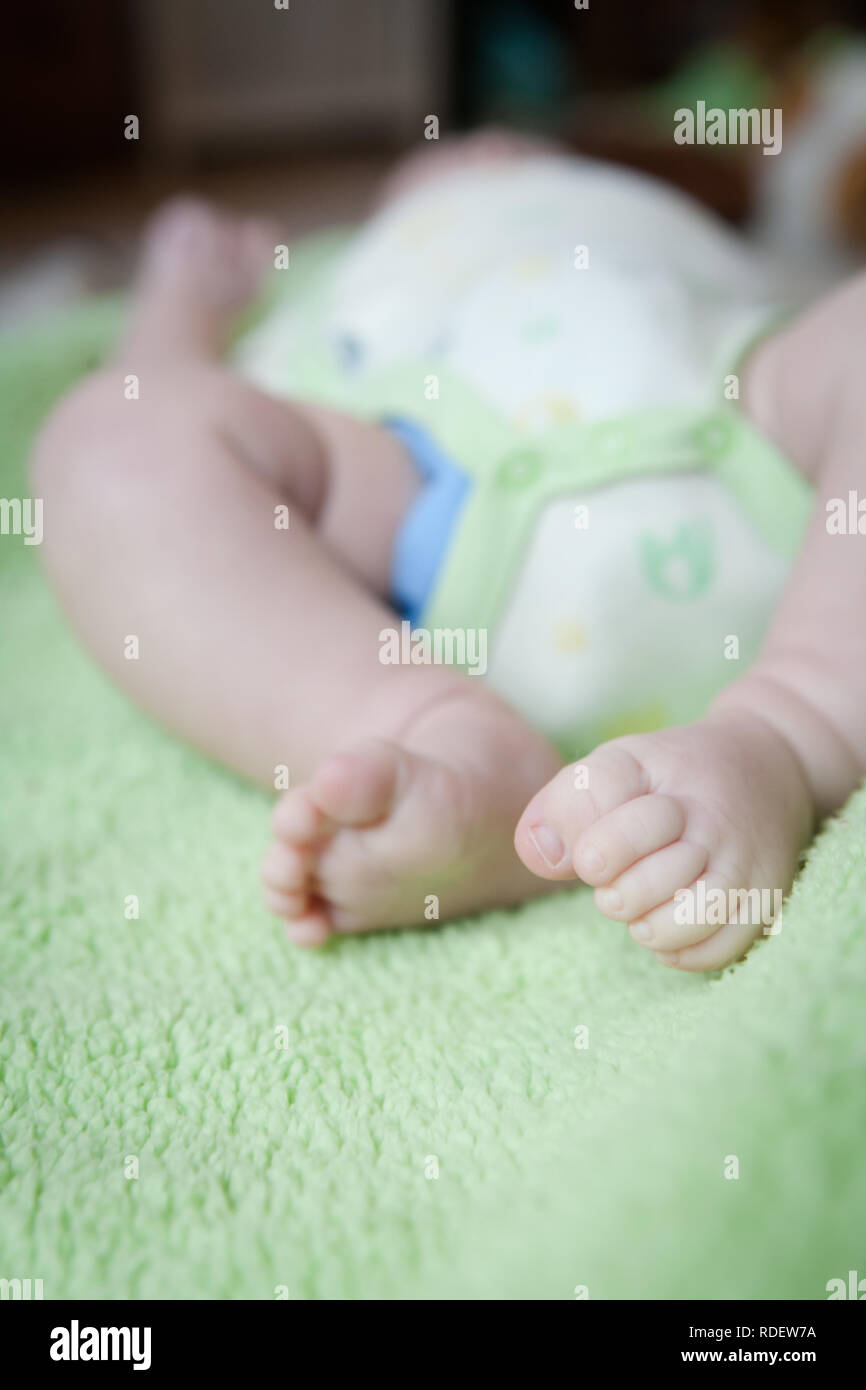 Ein Baby, das auf dem Rücken auf einer fuzzy grünen Decke liegt. Die Farben und die Kleidung sind geschlechtsneutral. Stockfoto