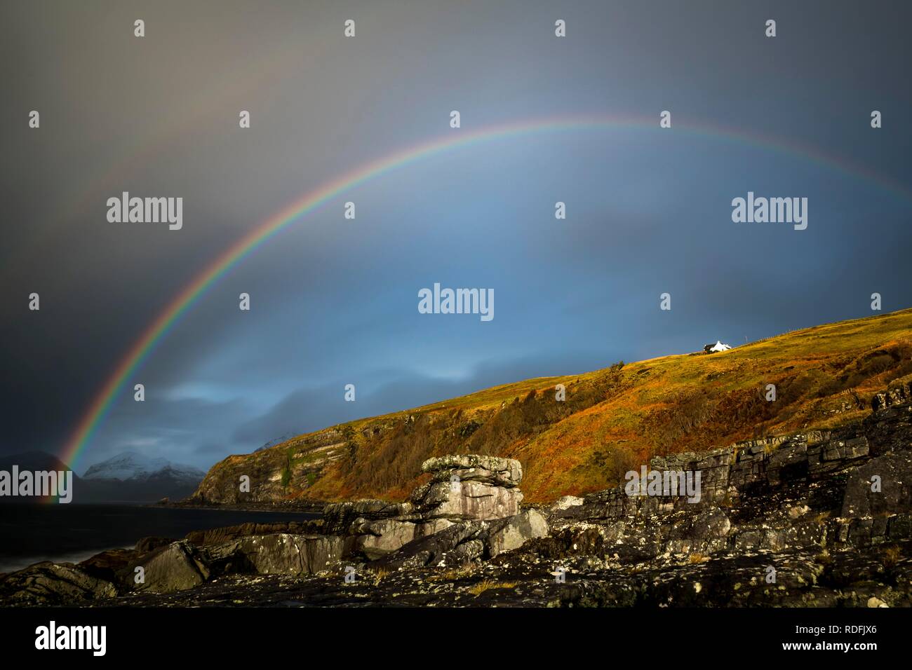 Großen Felsen im Wasser der Nordsee mit schneebedeckten Cullin Mountains und der Regenbogen im Hintergrund, Elgol, Isle of Skye, Schottland Stockfoto