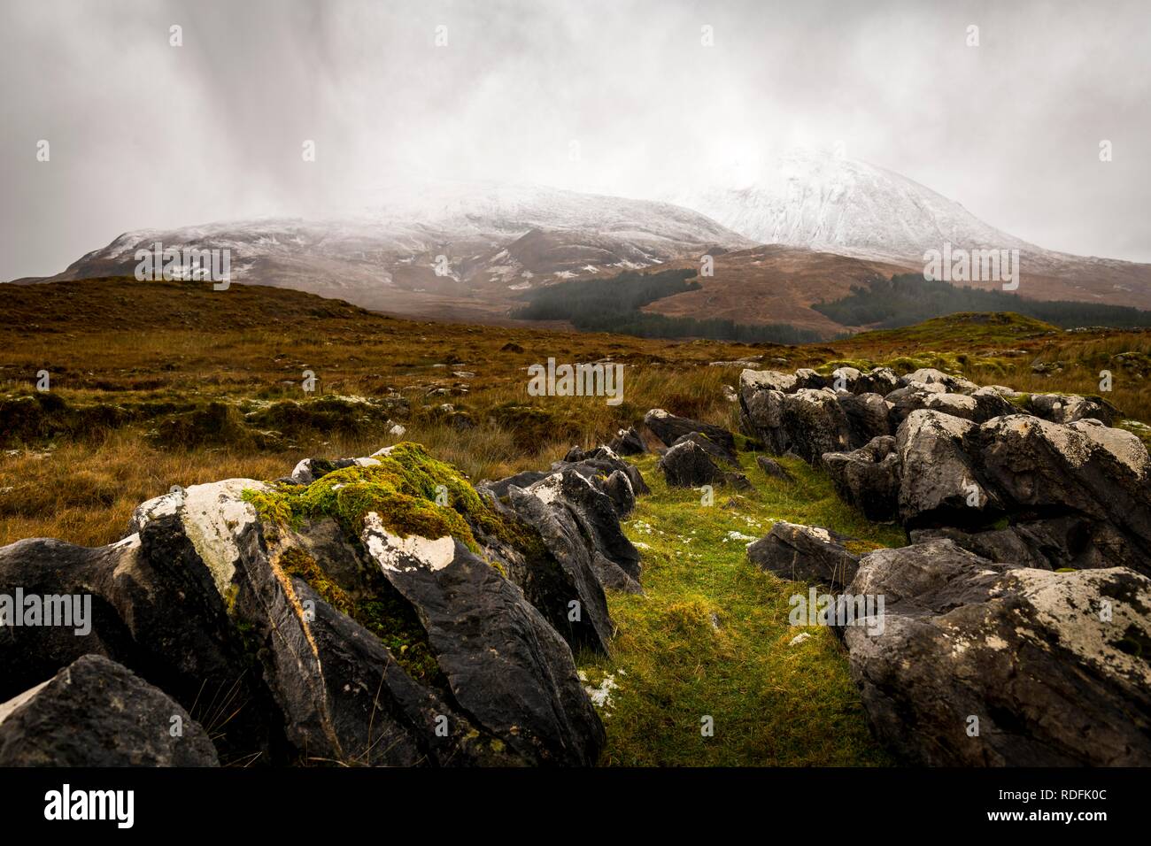 Dunkle Felsen mit weissen Kappen in Highland Landschaft mit schneebedeckten Cullin Mountains im Hintergrund, Broadford, Isle of Skye Stockfoto