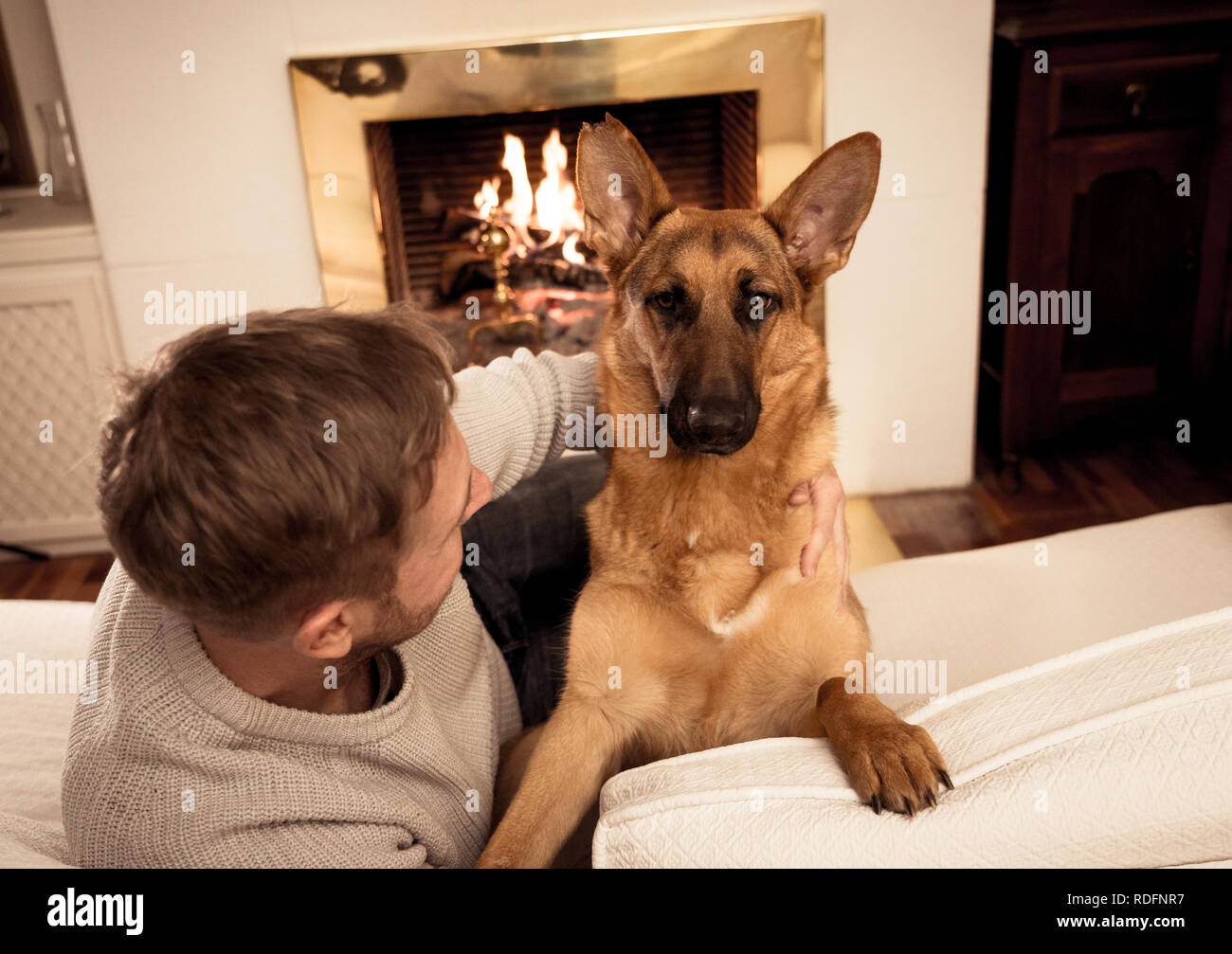 Schöne Portrait von lächelnden Mann umarmen Hund Schäferhund zusammen spielen vor dem Kamin in der gemütlichen Wohnung im Winter Tag in Glück radeln Stockfoto