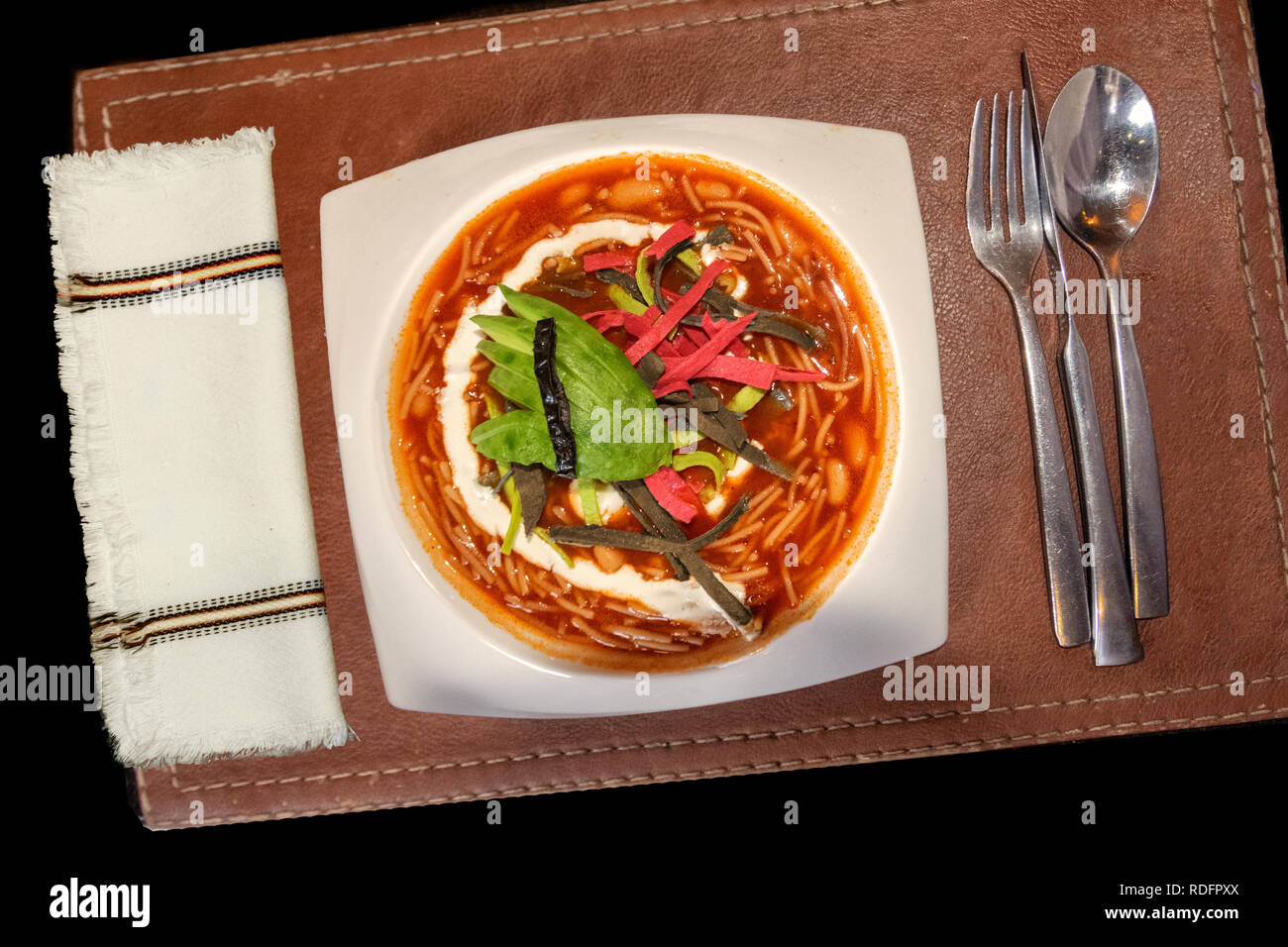 Festliche chipotle mexikanische Tortilla Soup garniert mit Avocado Schichten und Leder Tischset Stockfoto
