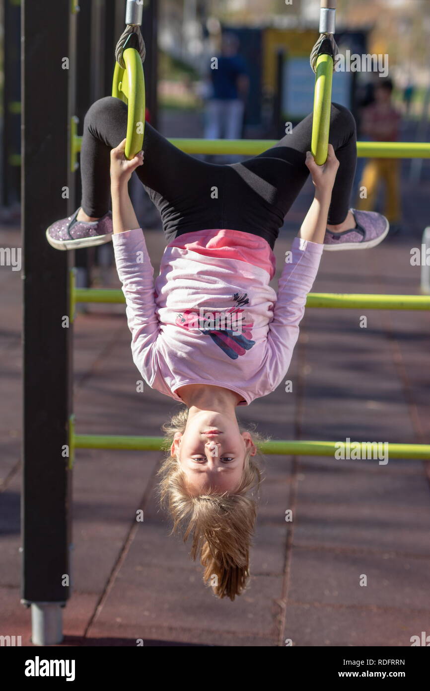 Junge Mädchen Ausübung auf Gymnastik Ringe kopfüber Position außerhalb auf einem Spielplatz Stockfoto