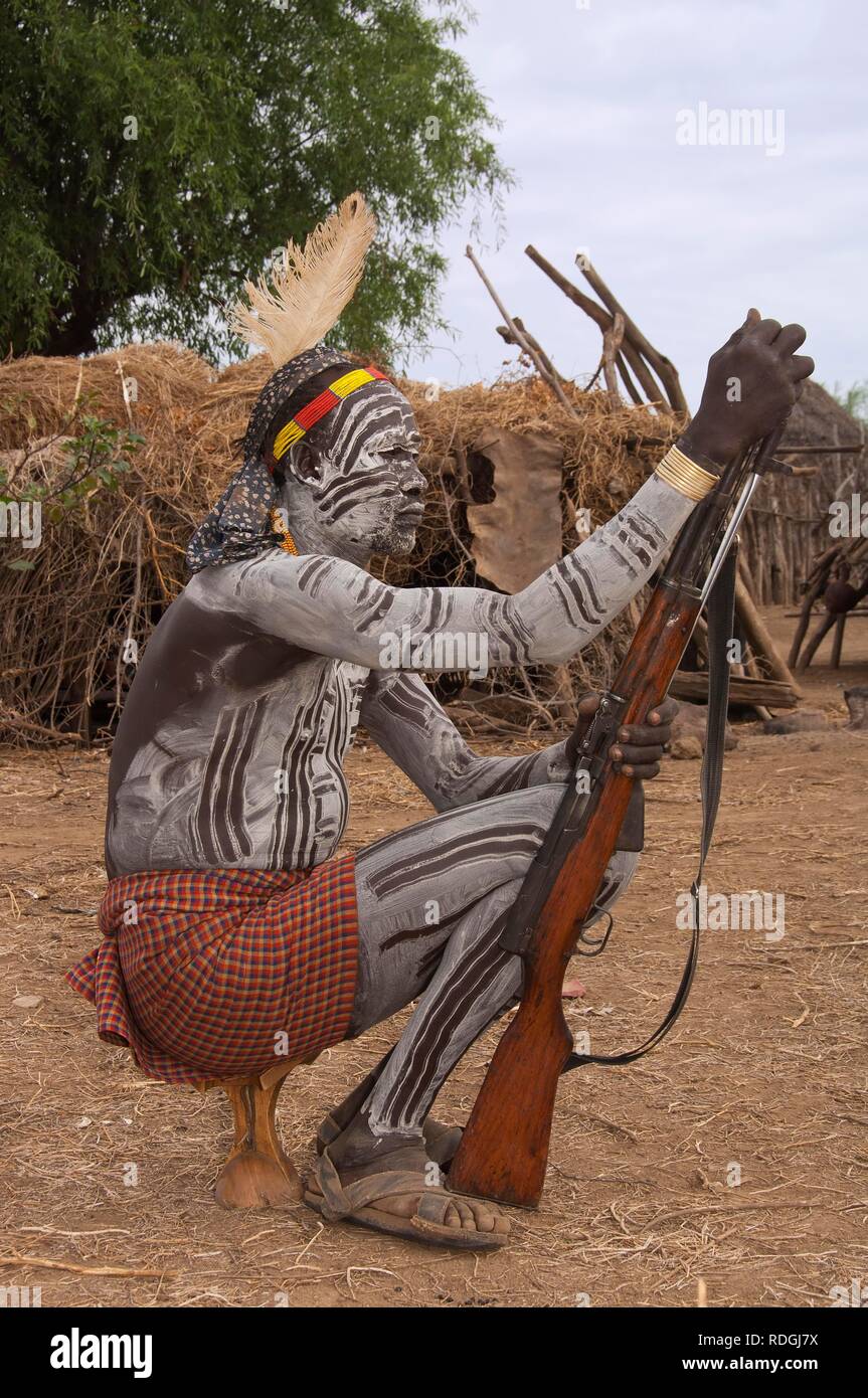 Karo Krieger mit Gesichts- und Gemälden und einem Gewehr auf seinem Sitz, Kopfstütze Omo-tal, südlichen Äthiopien, Afrika Stockfoto
