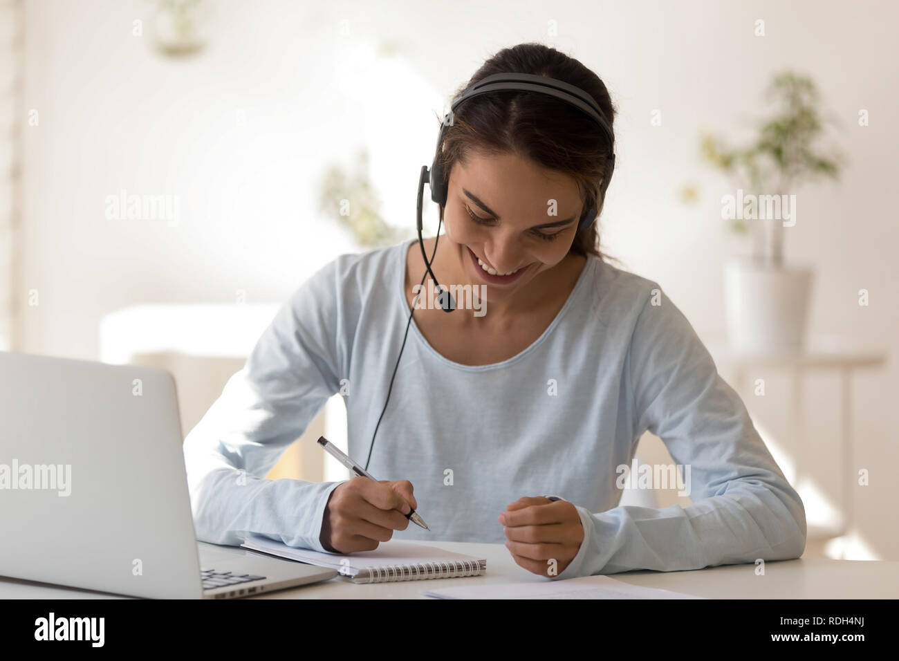 Glücklich lächelnde Frau in Kopfhörer schreiben Bekanntmachung im Notebook Stockfoto