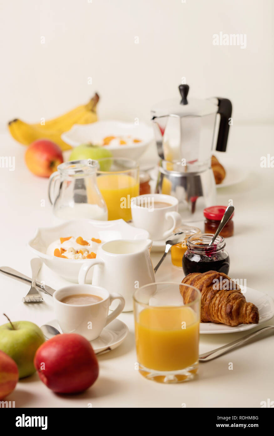 Zeit für das Frühstück. Orangensaft und Croissants, Marmelade und Honig. Kaffee mit Sahne oder Milch. Früchte wie Bananen, rote und grüne Äpfel. Ricotta mit Sauerrahm Stockfoto