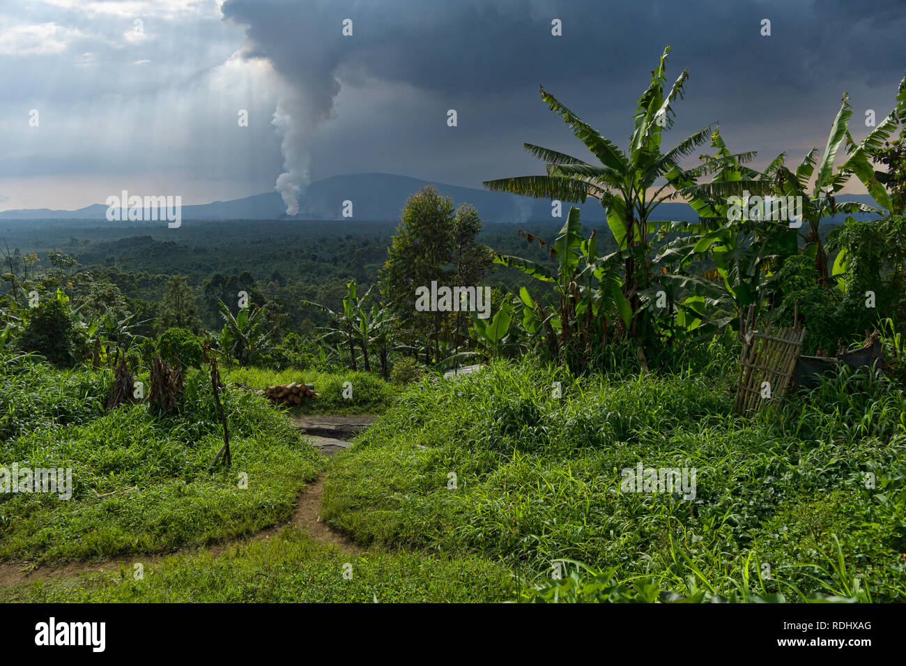 Nyamuragira, ein aktiver Vulkan, bricht in den Hintergrund eines ländlichen Dorfes im Virunga Nationalpark in der Demokratischen Republik Kongo. Stockfoto