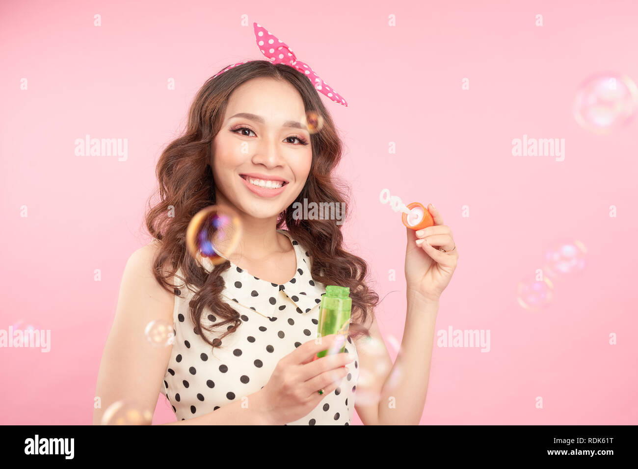 Verspielte Frau, Blasen, Blasen in die Kamera wie Sie feiert eine besondere Gelegenheit oder Geburtstag, über rosa Hintergrund Stockfoto