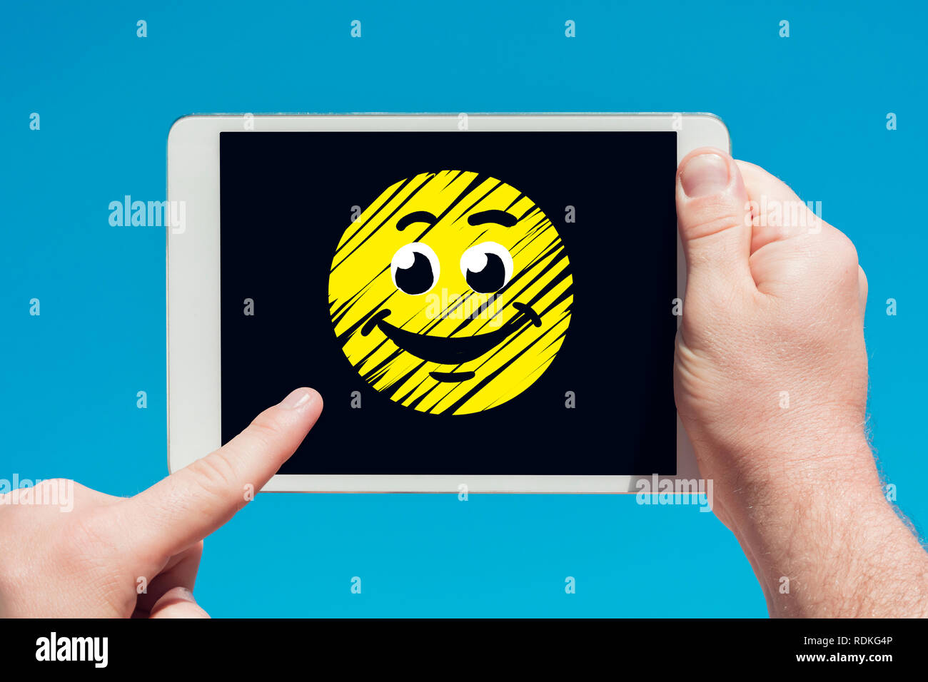 Mann hält eine Tablette ein lachendes Smiley Symbol und berühren Sie den Bildschirm mit einem Finger mit blauen Himmel im Hintergrund. Stockfoto