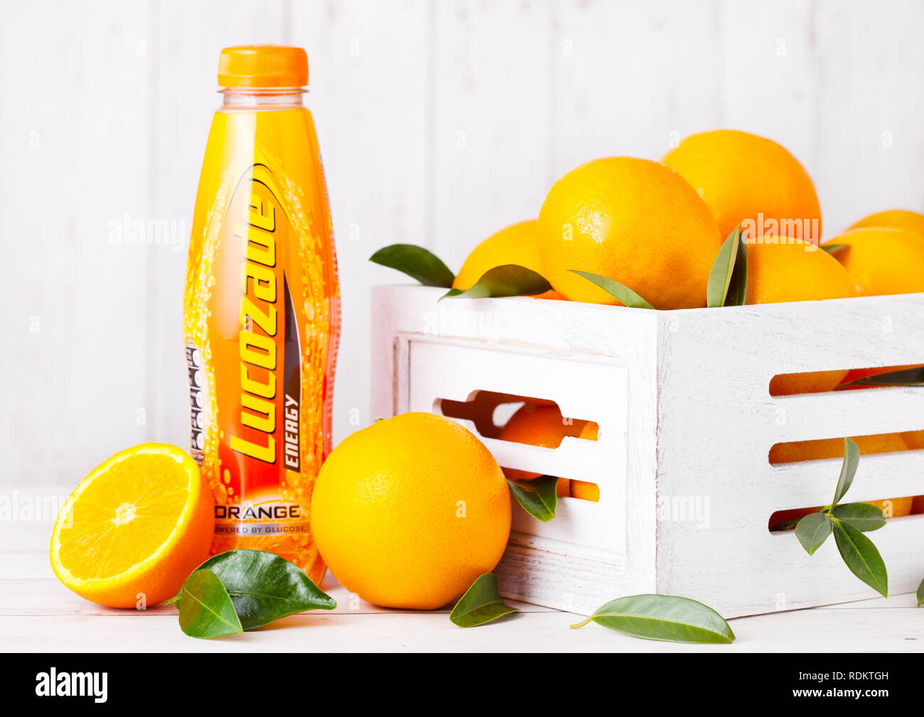 LONDON, Großbritannien - 15 Januar, 2019: Kunststoff Flasche Lucozade orange Soft soda Drink mit frischen, rohen Orangen in Holzkiste. Stockfoto