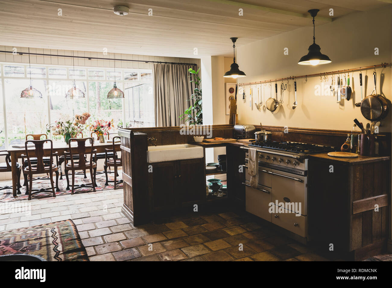 Innenansicht Küche mit Stein Fliesen, Herd und Spüle, bulter offen zu Wintergarten mit antiken hölzernen Esstisch und Stühlen. Stockfoto