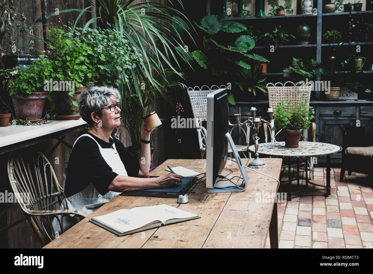 Ältere Frau Brille, schwarze und weisse Schürze an einem Holztisch sitzen, arbeiten auf dem Desktop Computer. Stockfoto