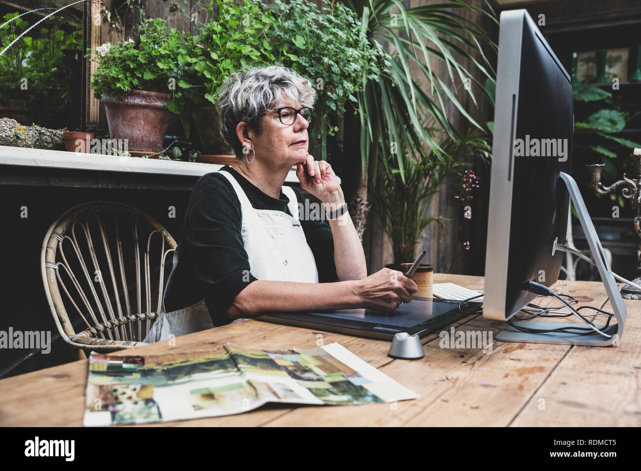 Ältere Frau Brille, schwarze und weisse Schürze an einem Holztisch sitzen, arbeiten auf dem Desktop Computer. Stockfoto