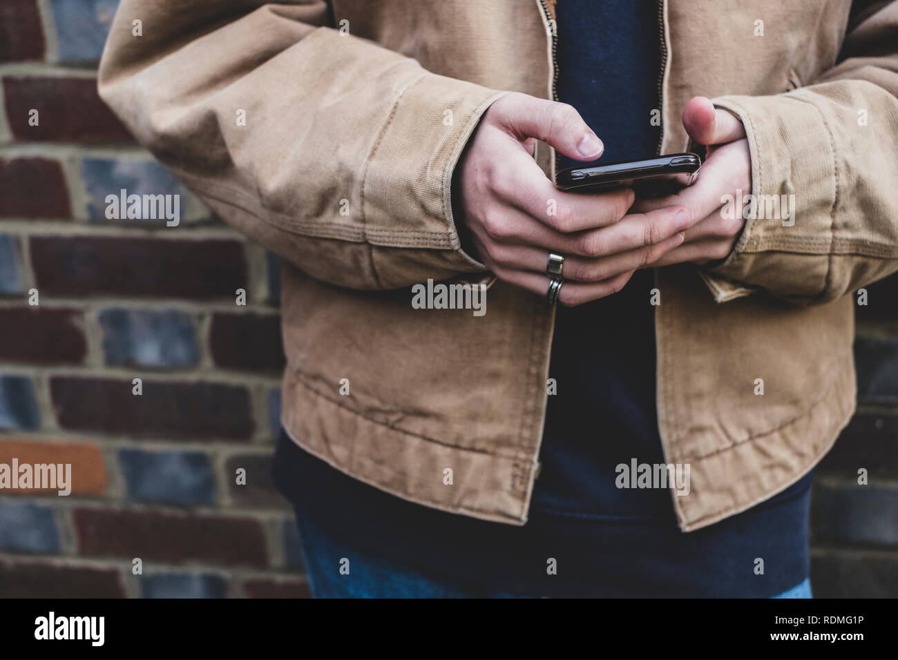 Der junge Mann legere Jacke stehen gegen eine Mauer, SMS auf sein Handy. Stockfoto
