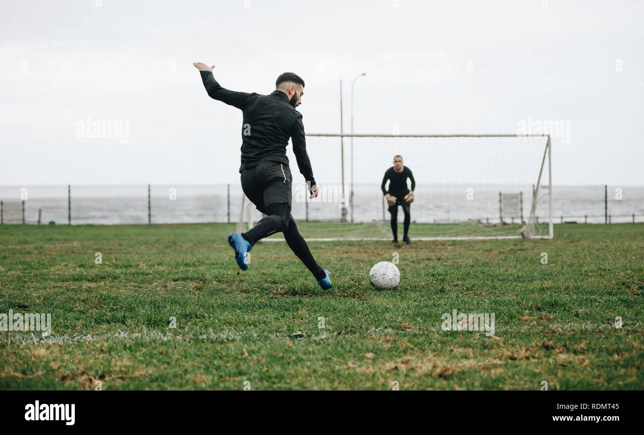 Der Fußballer schlägt einen Elfmeterschuss. Fußballspieler tritt den Ball in Richtung Torpfosten, während sich der Torwart in Position befindet. Stockfoto