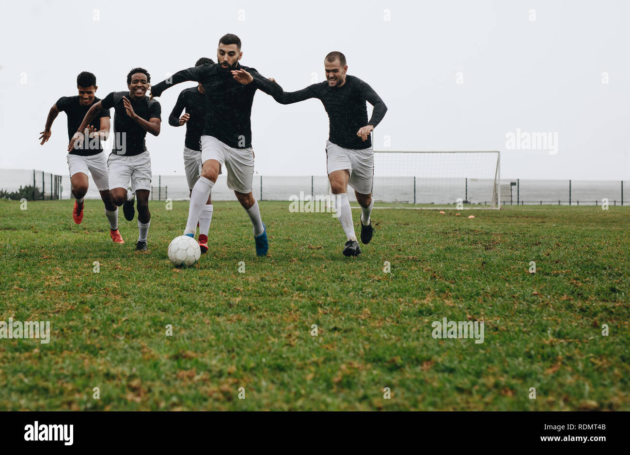 Fußballspieler üben morgens auf dem Feld. Fußballer, der mit dem Ball tritt und läuft, während andere Spieler hinter sich herrennen, um Besitz zu erlangen. Stockfoto