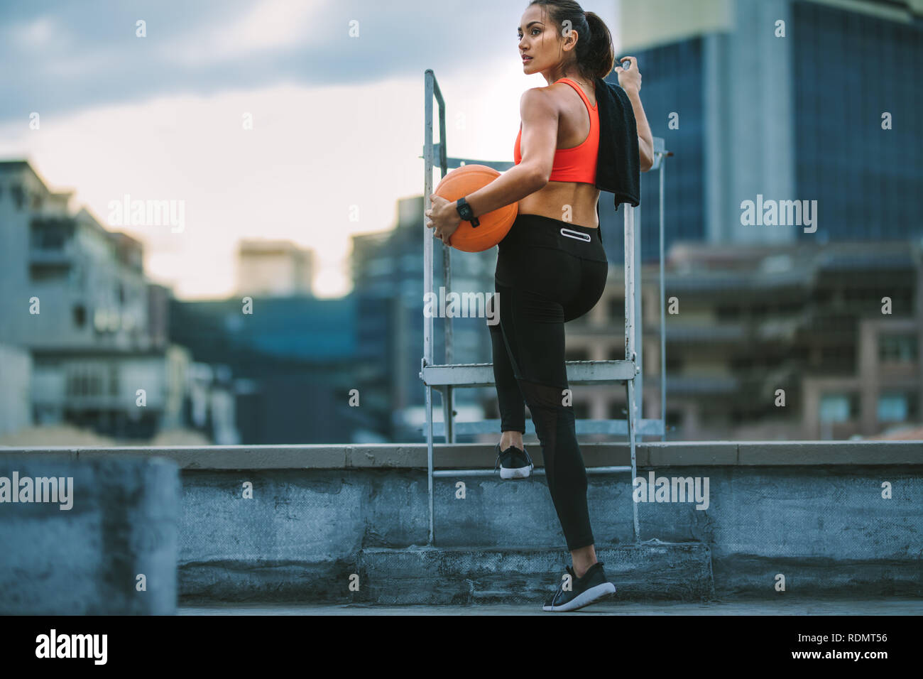 Frau in fitness Verschleiß auf der Dachterrasse mit einem Basketball. Rückansicht eines Fitness Frau in der Nähe einer Treppe auf dem Dach stehend und Wegsehen. Stockfoto