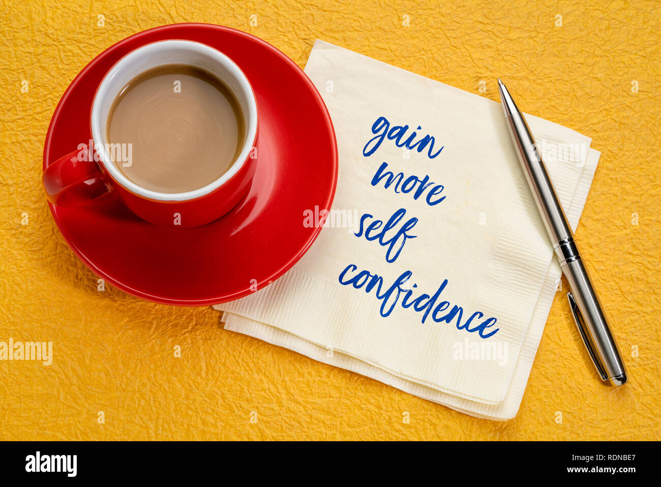 Gewinnen Sie mehr Selbstvertrauen - Handschrift auf eine Serviette mit einer Tasse Kaffee Stockfoto