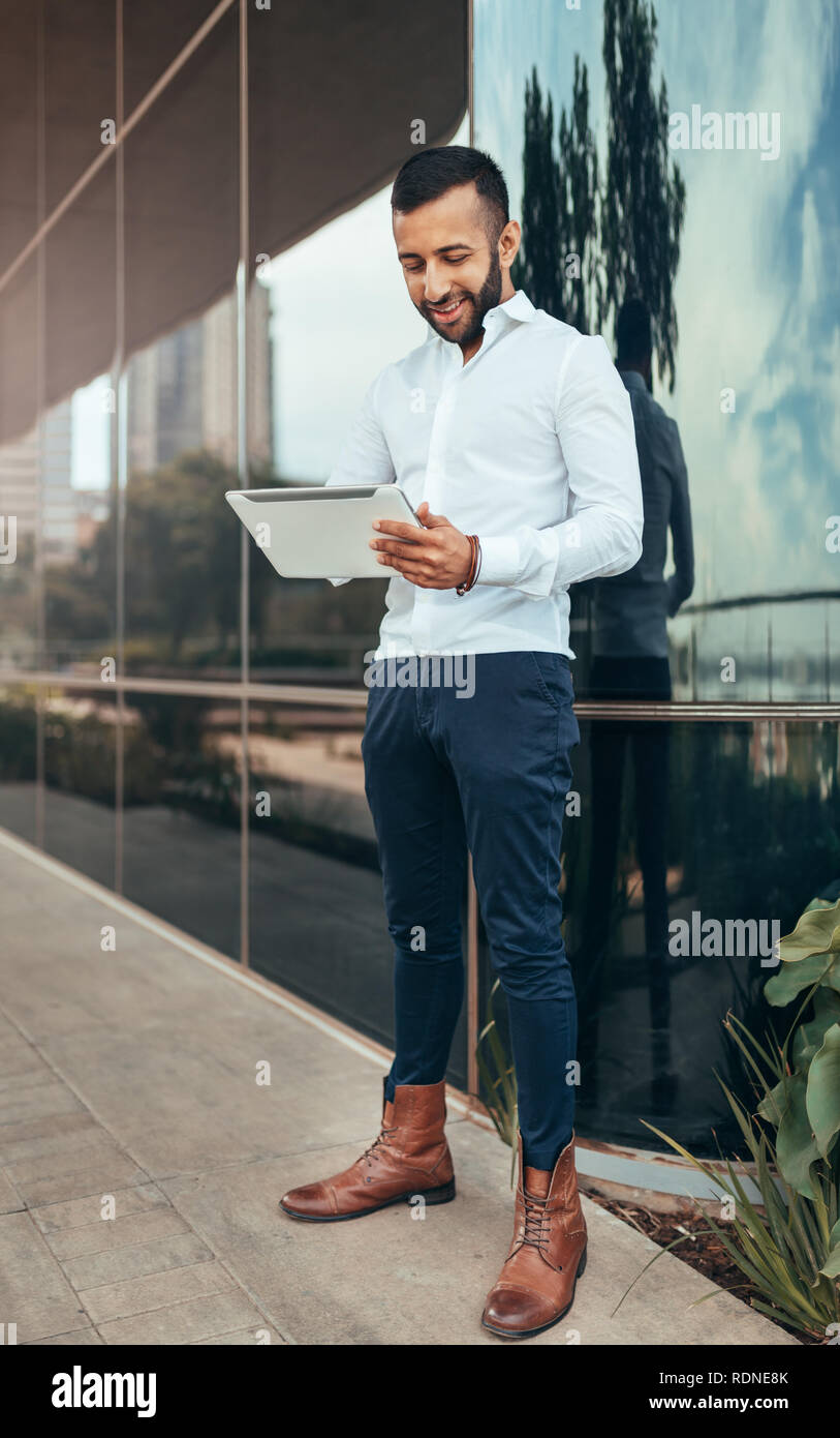 Portrait einer jungen zuversichtlich trendy indischen Mann stand und halten ein Tablet Stockfoto