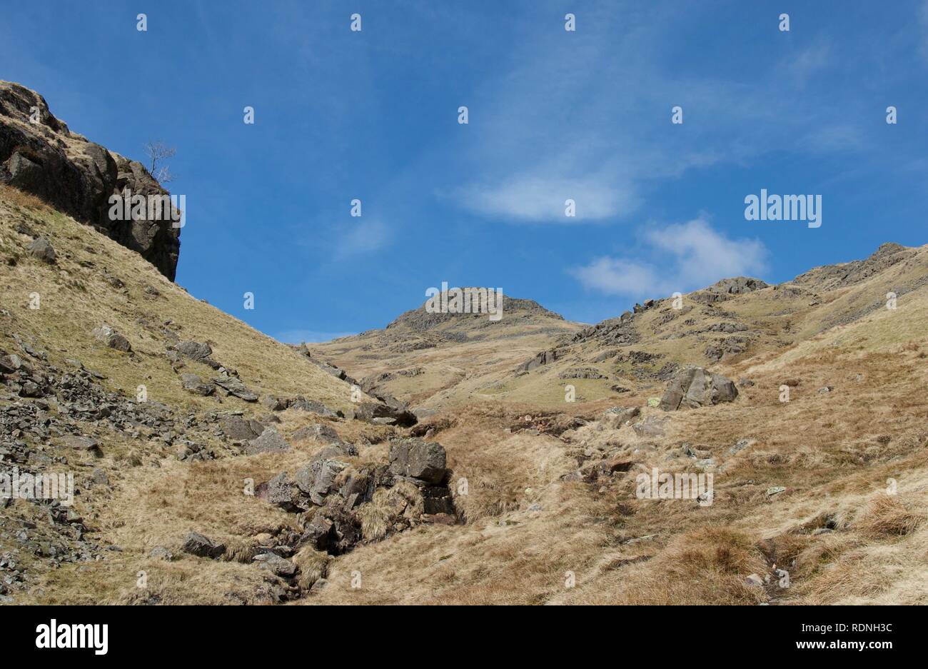 Breite Tal zwischen Felsen: Mountain Stream (Beck) zwischen Felsen und grünen Heide. Blauer Himmel mit weißen Wolken, Felsen und einige Berggipfel. Foo Stockfoto