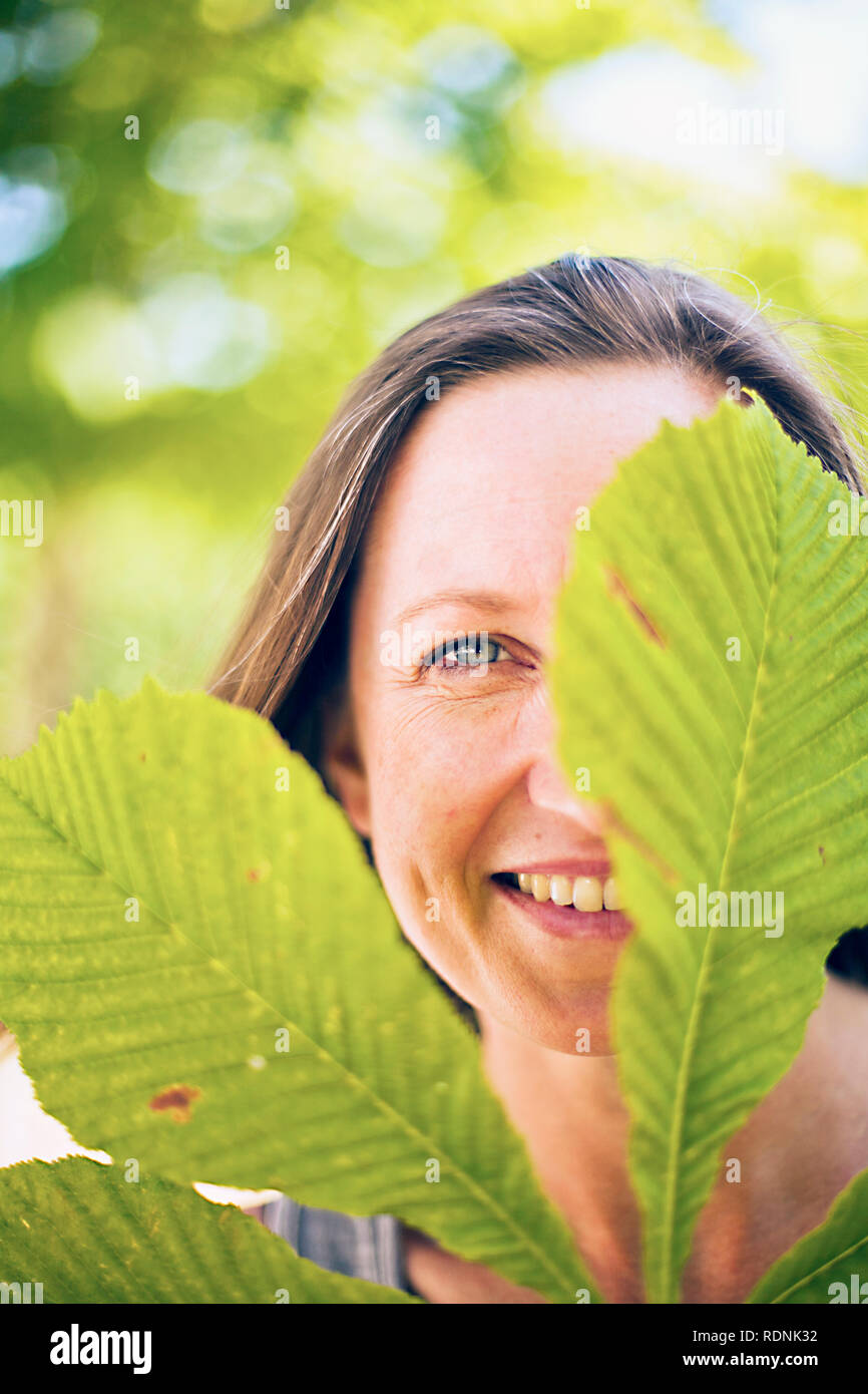 Porträt der lächelnde Frau mit Kastanien Blatt im Vordergrund Stockfoto