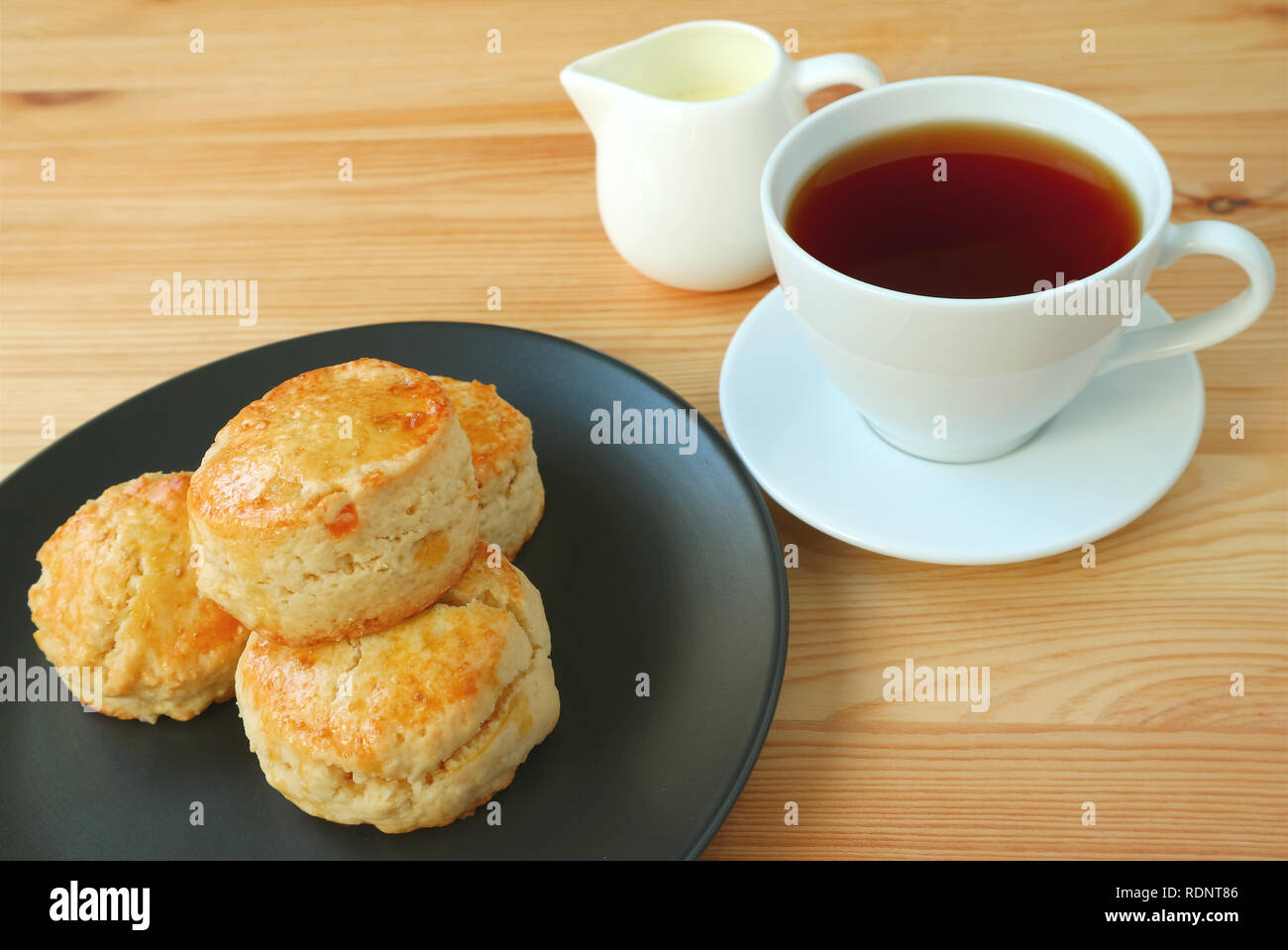 Eine Platte mit orangeat Scones und eine heiße Tasse Tee serviert auf hölzernen Tisch Stockfoto
