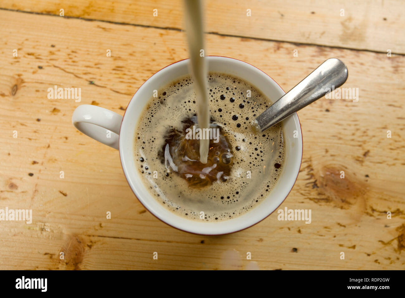 Ansicht von oben von Milch in die Kaffeetasse gegossen wird, Stockfoto