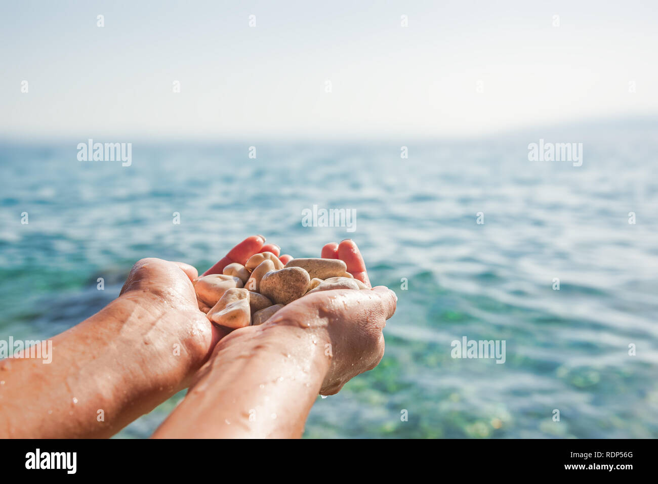 Weibliche Hände auf dem Hintergrund von Meer oder Ozean halten Meer Steine. Stockfoto