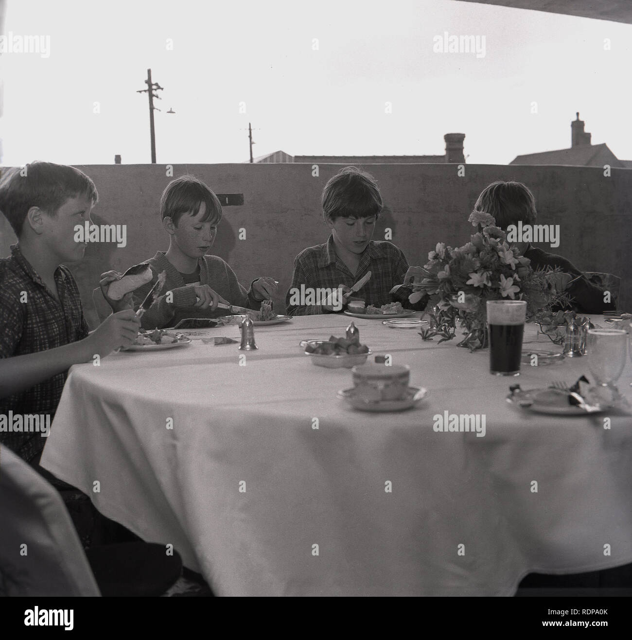 1967, historische, vier junge Jungen, die einen ausgefallenen Tee auf einem mit Stoff bedeckten Tisch an einem ungewöhnlichen Ort haben... die oberste Etage eines mehrstöckigen Parkplatzes, organisiert vom gemeinderat zur Feier seiner Eröffnung, England, Großbritannien. Stockfoto