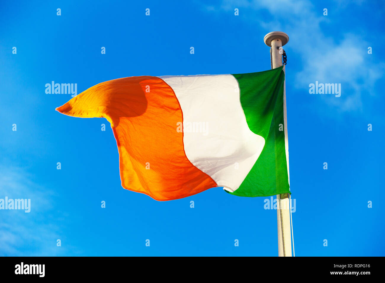 Die irische Flagge im Wind vor blauem Himmel. Stockfoto