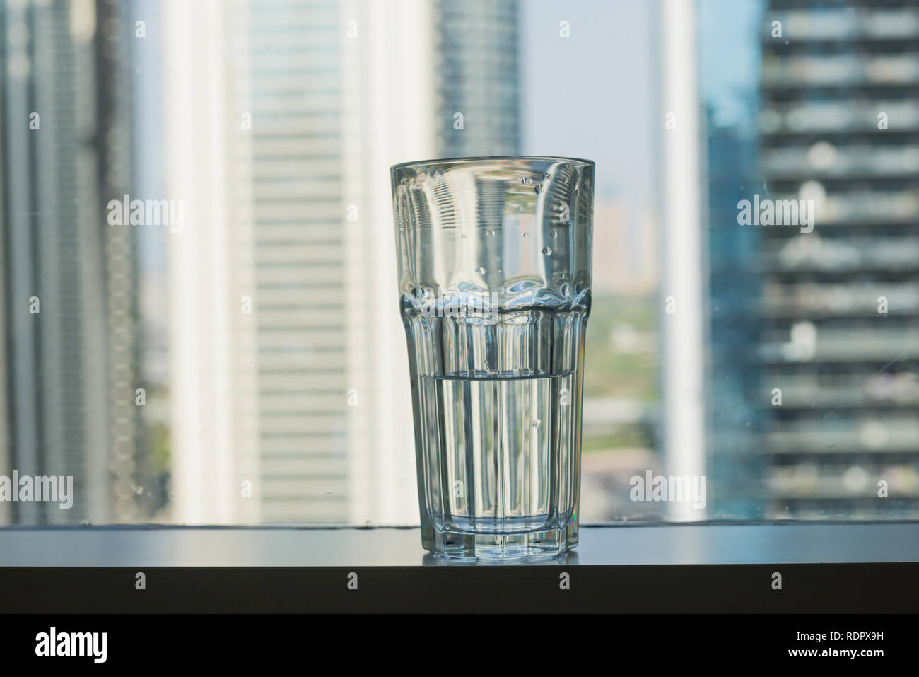 Ein halb gefüllten Glas Wasser gegen Fenster mit Skyline im Hintergrund platziert. Die Freifläche mit einer Überschrift zu schreiben. Stockfoto