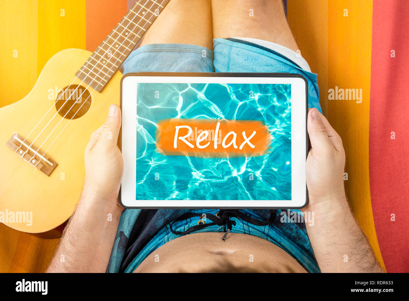 Junger Mann auf einer Hängematte mit tablet device an Wasser Hintergrund mit dem Wort "Relax" geschrieben, die lügen. Stockfoto