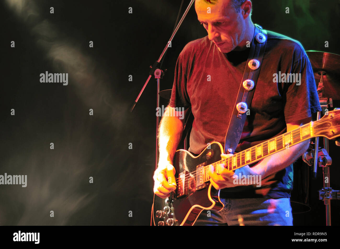 Gitarrist spielt E-Gitarre auf der Bühne mit Rauch und Licht ein Drum Kit ist teilweise hinter dem Performer sichtbar. Es ist dunkel negativen Raum. Stockfoto