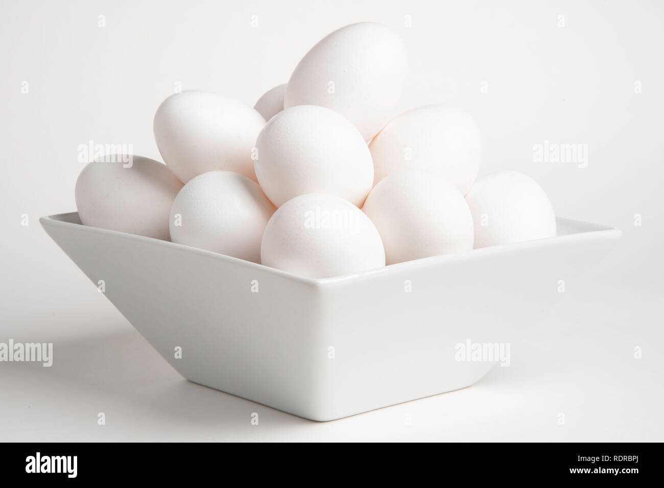 Ein Bündel weißer rohe Eier auf einer tiefen Platz Schüssel gegen einen weißen Hintergrund in horiontal Bildformat eingestellt gestapelt. Stockfoto