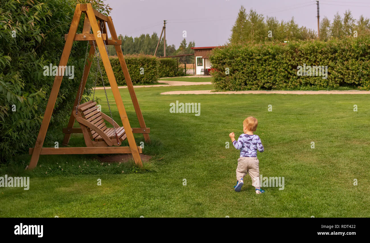 Kleines Kind gegenüber Holz schaukel Bank im Park läuft. Kinder spielen im  Garten Stockfotografie - Alamy
