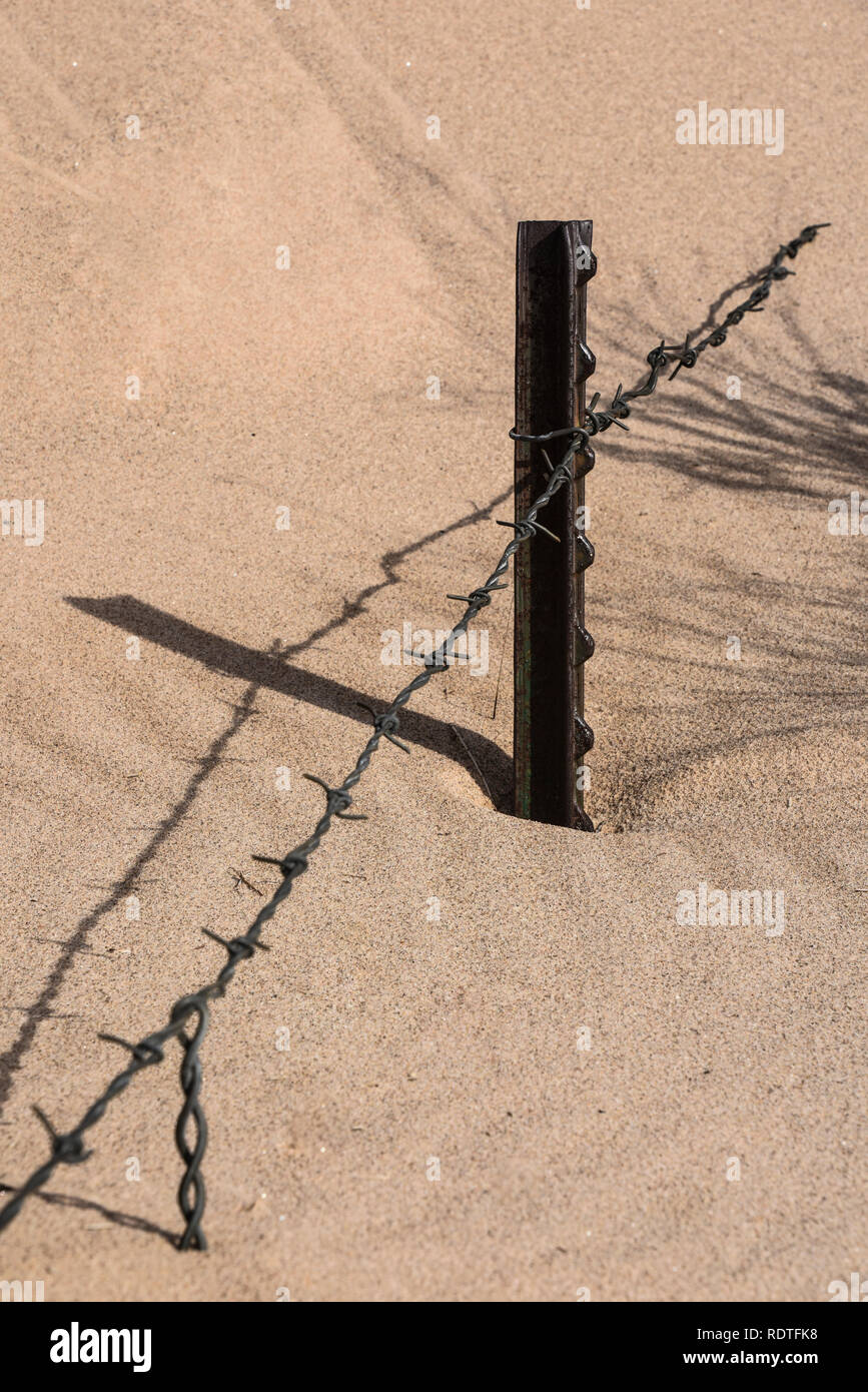 Stacheldraht zaun mit Metall Beiträge fast im Sand begraben Stockfoto