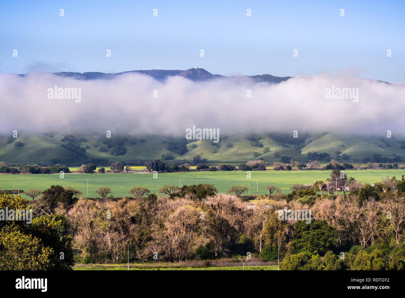 Blick auf die Spitze des Mt Umunhum und der Ehemaligen radar Gebäude, steigen über eine Schicht von Wolken; grüne Felder im Vordergrund sichtbar; South San Fr Stockfoto