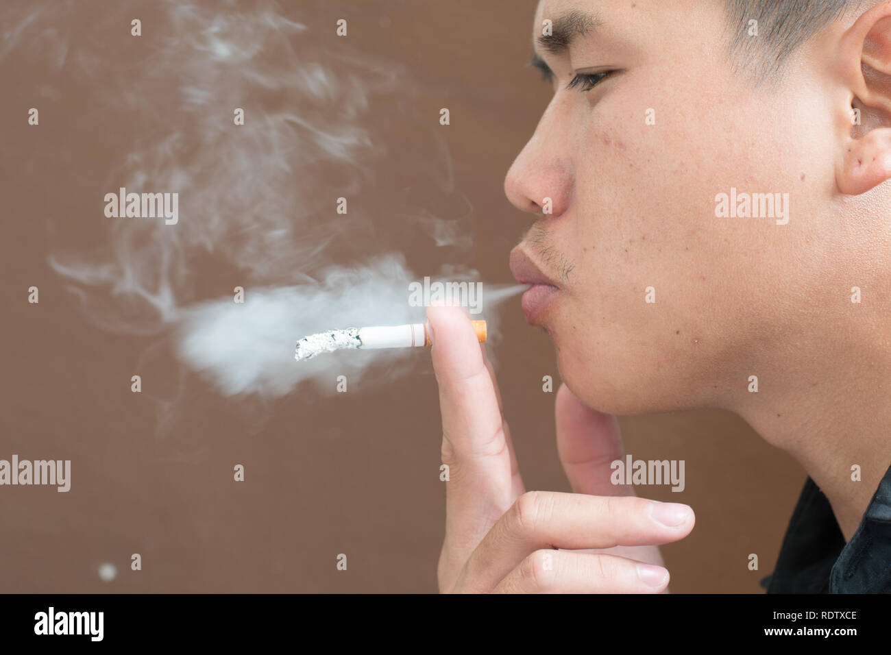 Seitenansicht des jungen Mannes ist Rauchen gegen braunen Hintergrund. Stockfoto