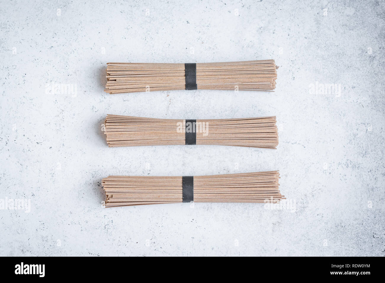 Soba Nudeln - traditionelle asiatische Lebensmittel Zutat. Bündel von Buchweizen Soba Nudeln auf Weiß konkreten Hintergrund, Ansicht von oben, kopieren. Stockfoto