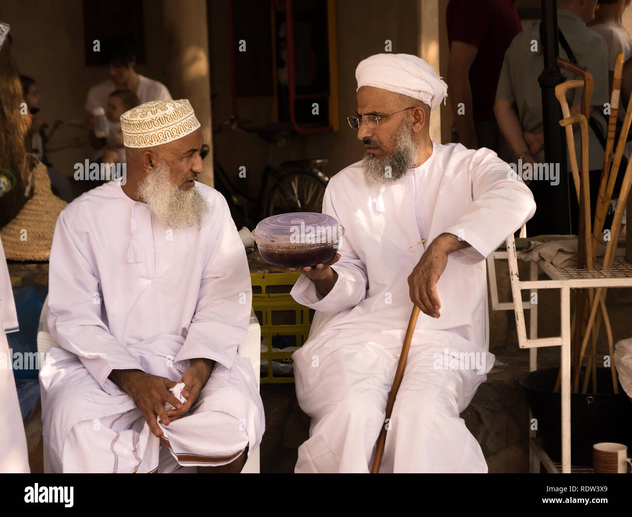 Nizwa, Oman - November 2, 2018: Omani mann Hände Halwa pack mit einem anderen Mann in traditioneller Kleidung am Nizwa Markt Stockfoto