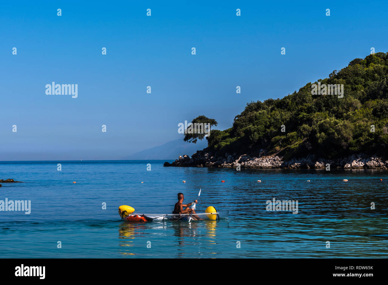 Ansicht der Rückseite ein junger Mann in einem Boot paddeln gezielt auf eine idyllische Insel, Sarande, Albanien Stockfoto