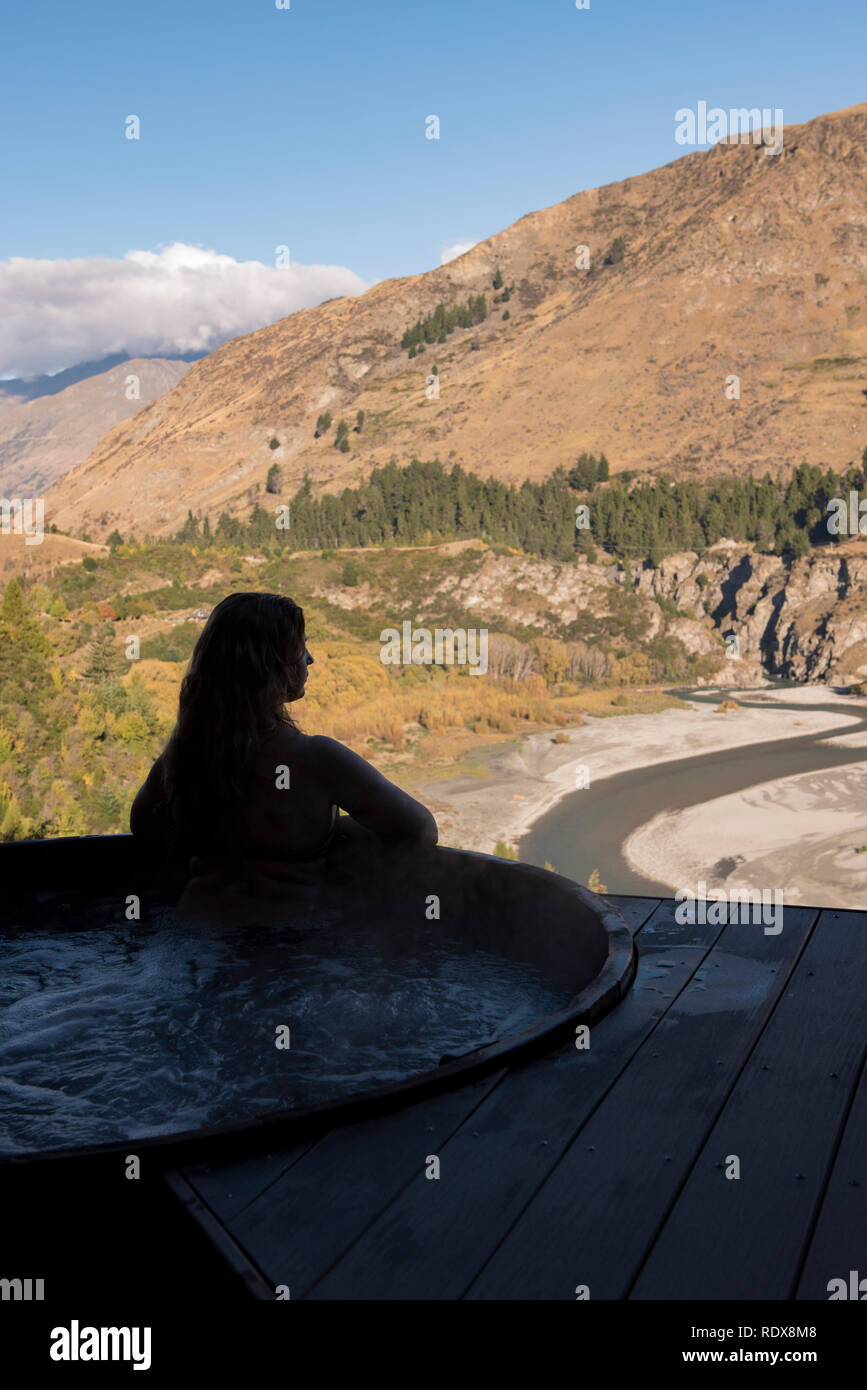 Eine Frau (Model Released) entspannt im Whirlpool mit Blick auf den Shotover River am Onsen Hot Pools in der Nähe von Queenstown, Neuseeland. Stockfoto