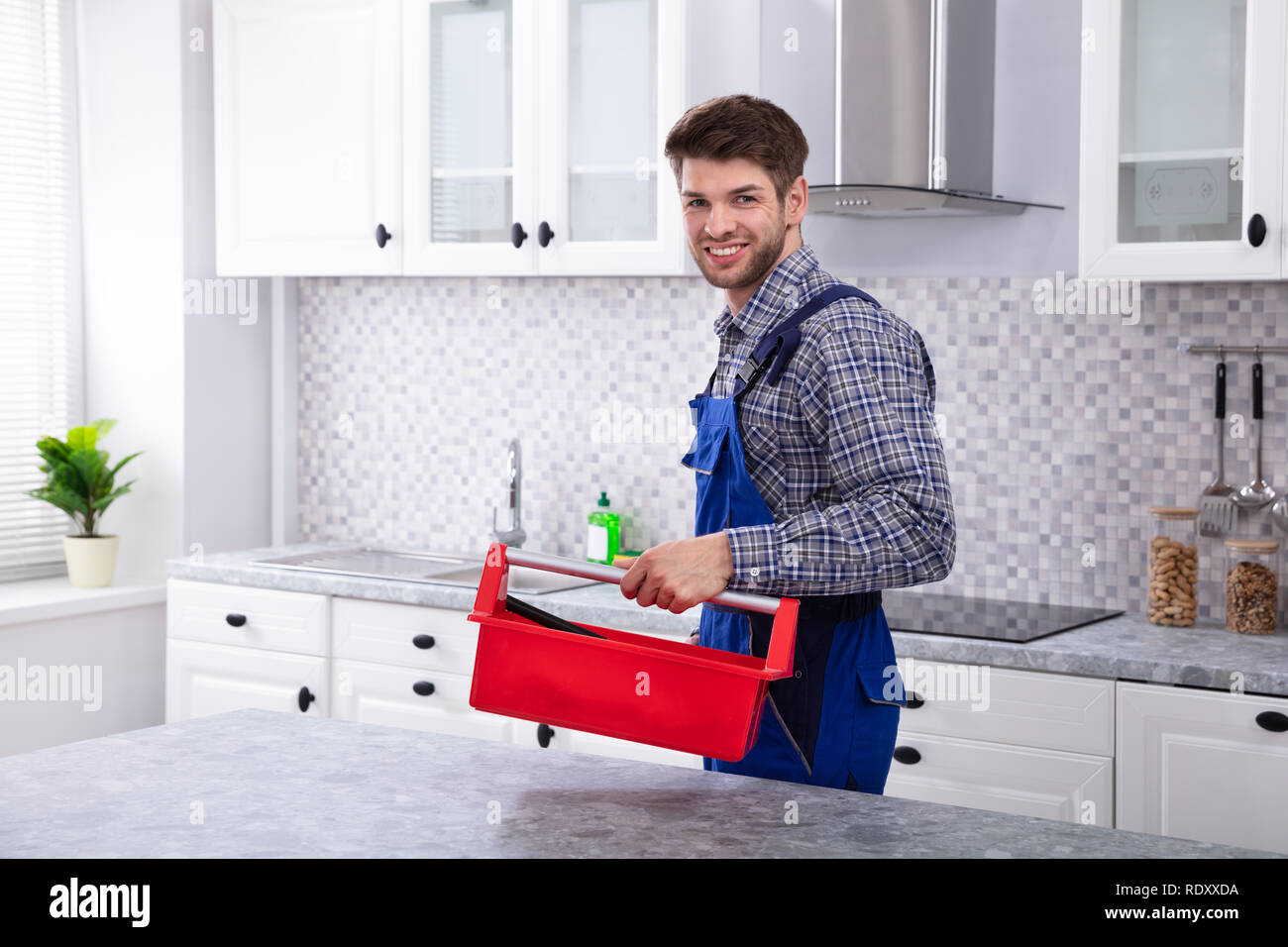 Gerne männliche Handwerker mit Red Toolbox stehen in der Küche Stockfoto