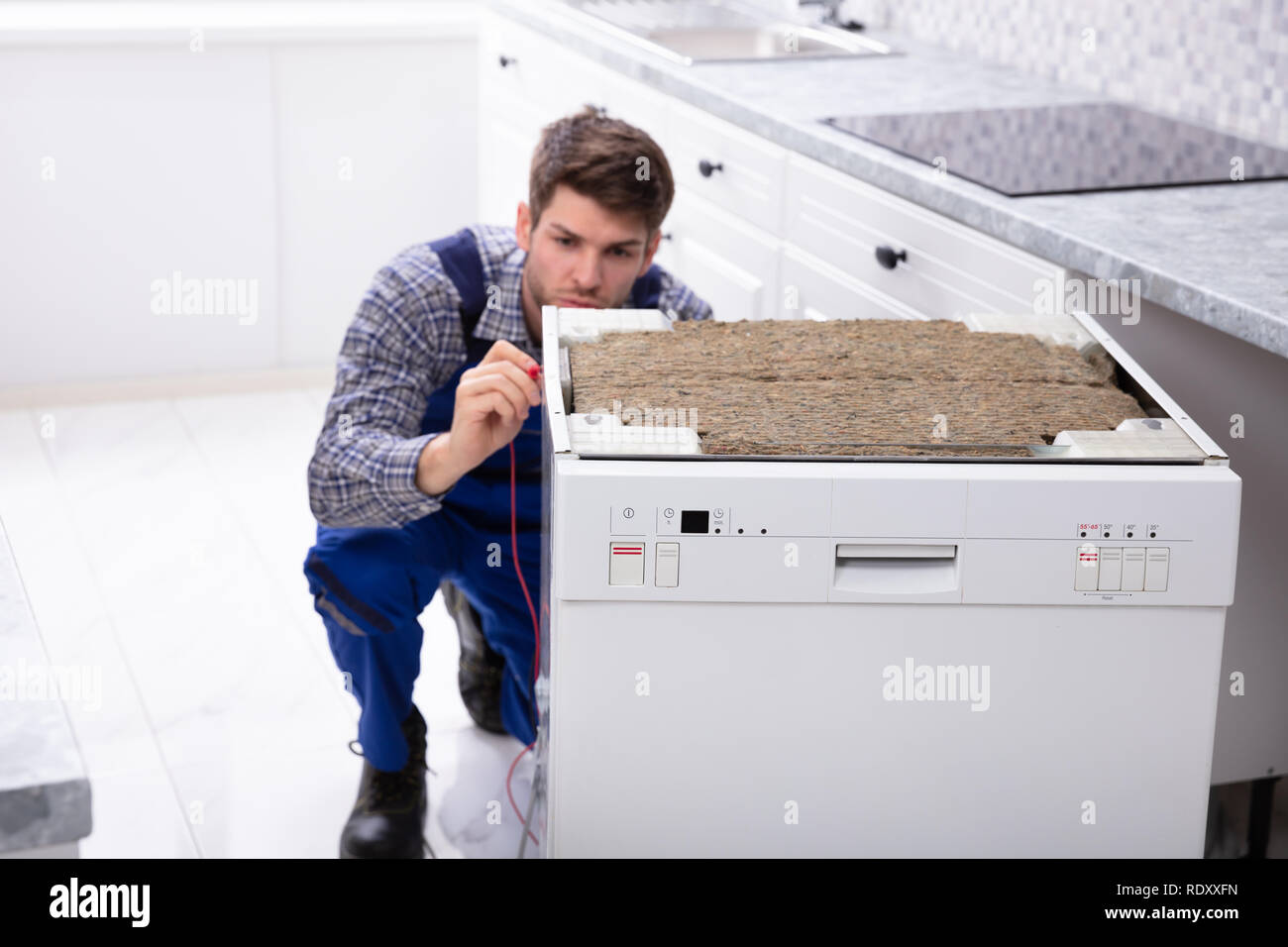 Junge männliche Techniker Reparatur Geschirrspüler in der Küche Stockfoto