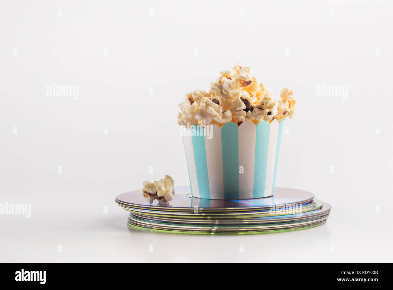 Miniatur-Eimer Popcorn auf einem Haufen Film-DVDs platziert. Ein Konzept für Home Entertainment. Verführerisches Popcorn im Papierbecher. Stockfoto