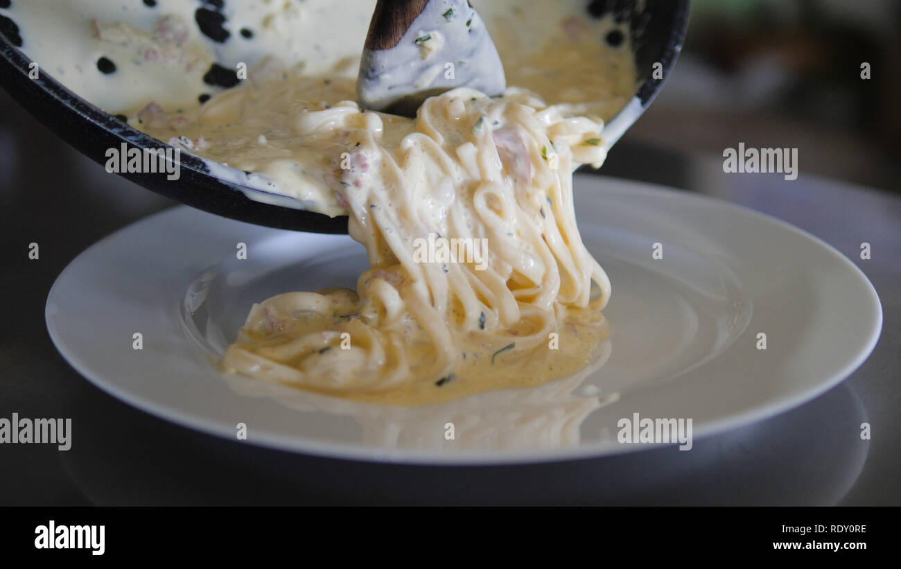 Cook gießt Spaghetti aus der Pfanne Spaghetti Carbonara. Konzept Stockfoto