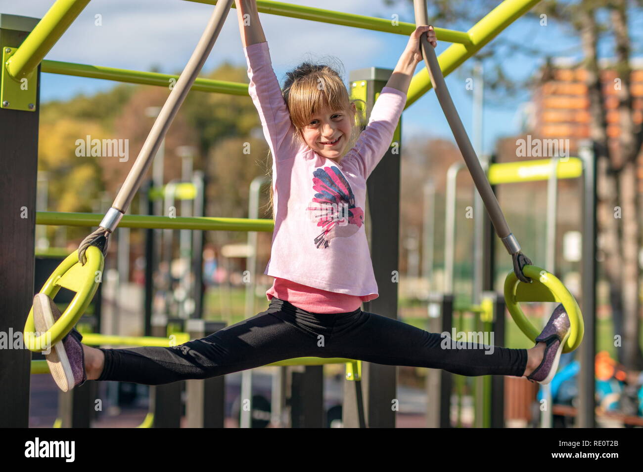 Junge Mädchen erstreckt sich in Splits Position auf Gymnastik Ringe außerhalb auf einem Spielplatz Stockfoto