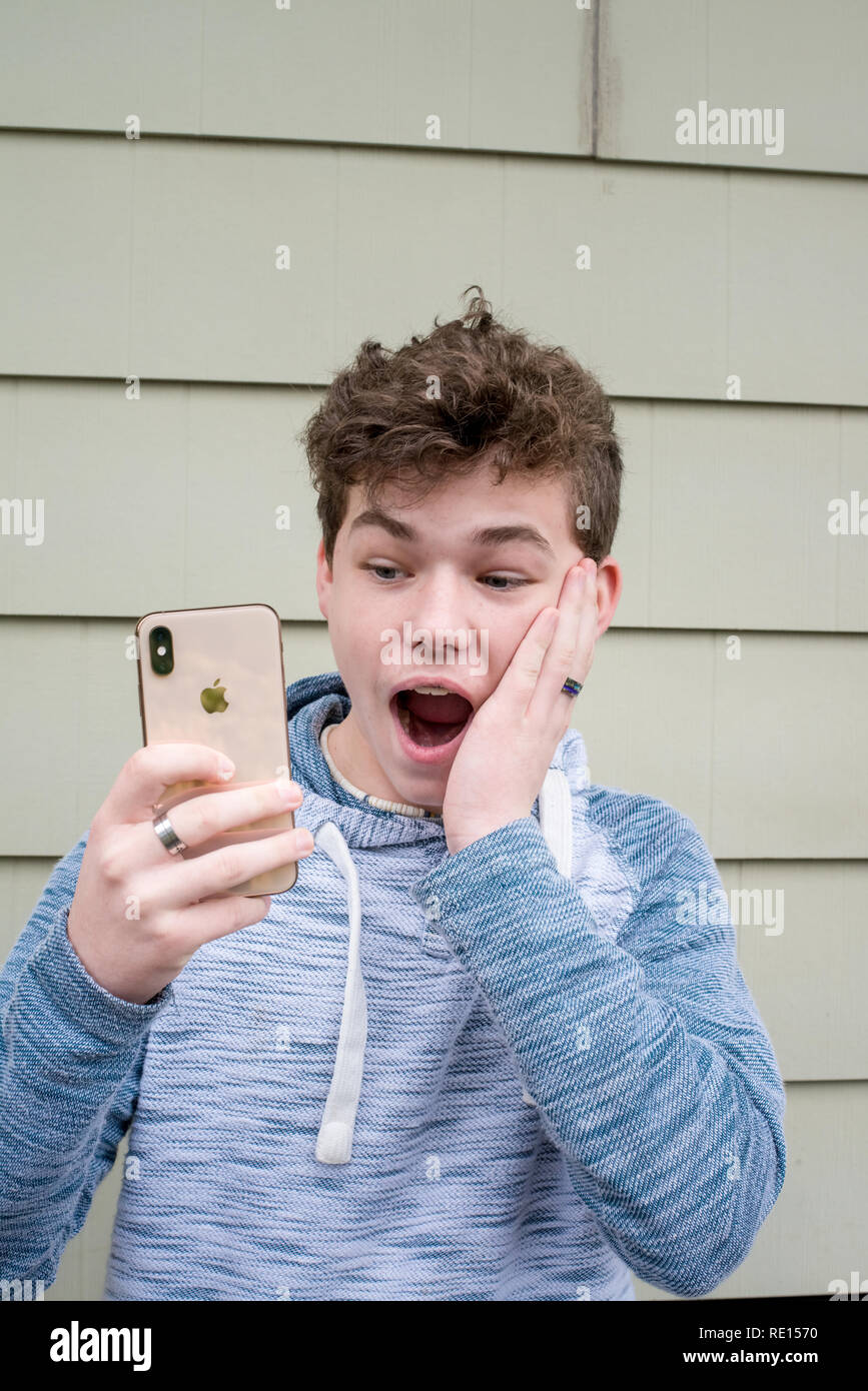 Cute teen Boy, lustige Gesichter während an seinem iPhone X neue Technologie suchen Stockfoto